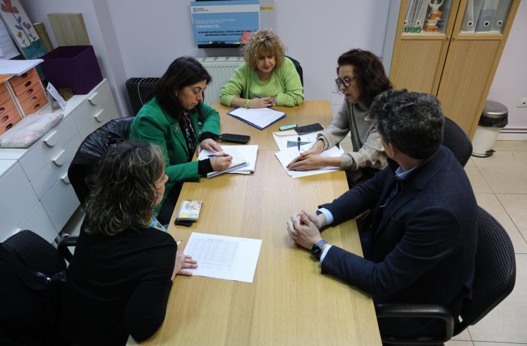 Reunión de seis personas alrededor de una mesa, discutiendo documentos y tomando notas.