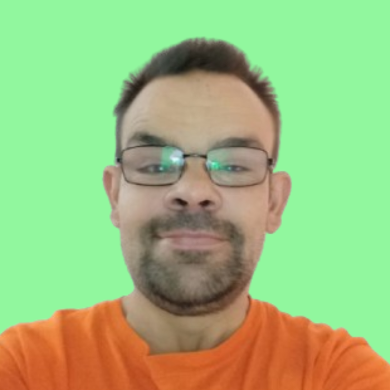 Hombre sonriente con gafas, camiseta naranja y fondo verde.